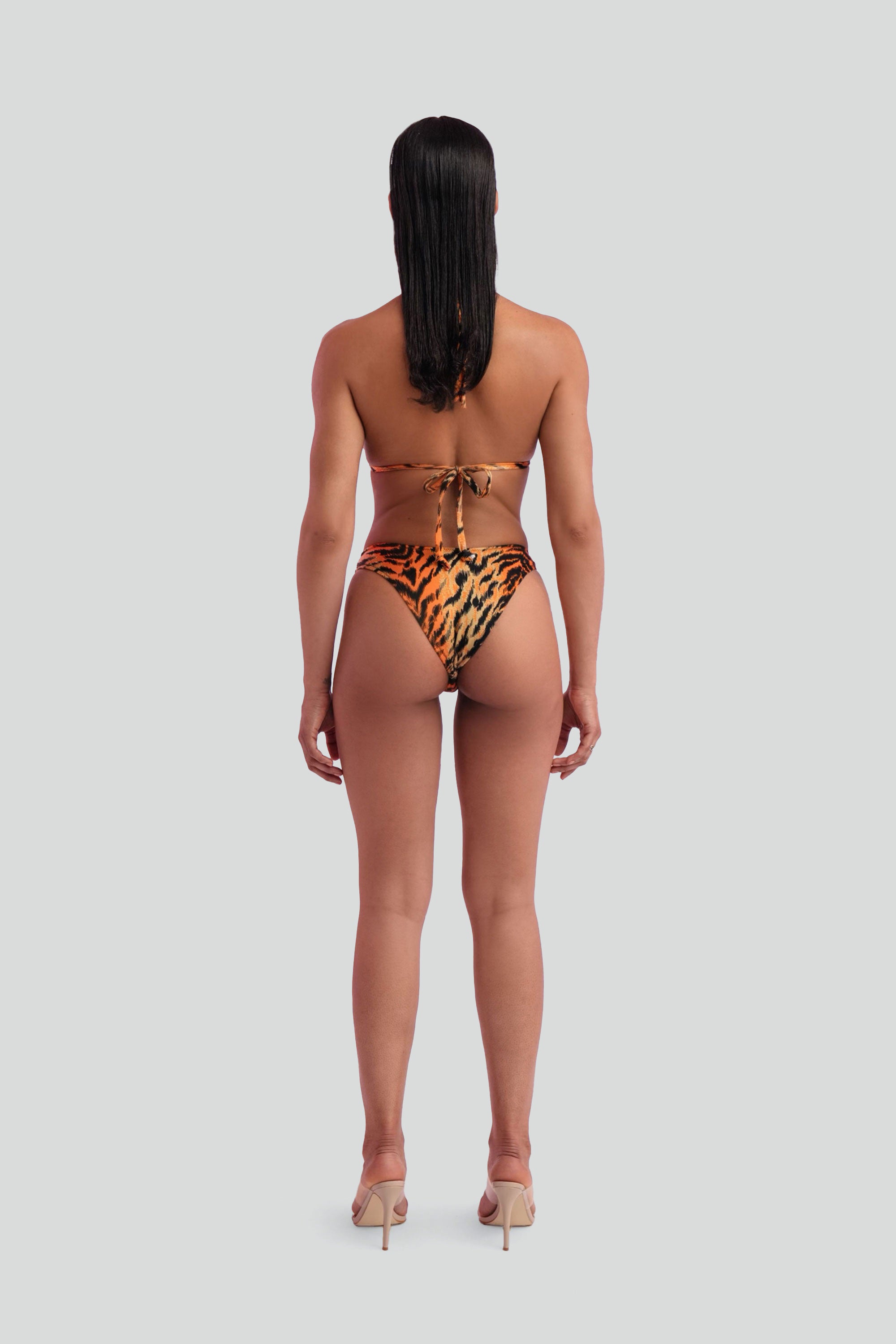 Back view of a woman wearing a tiger print triangle bikini on a white background