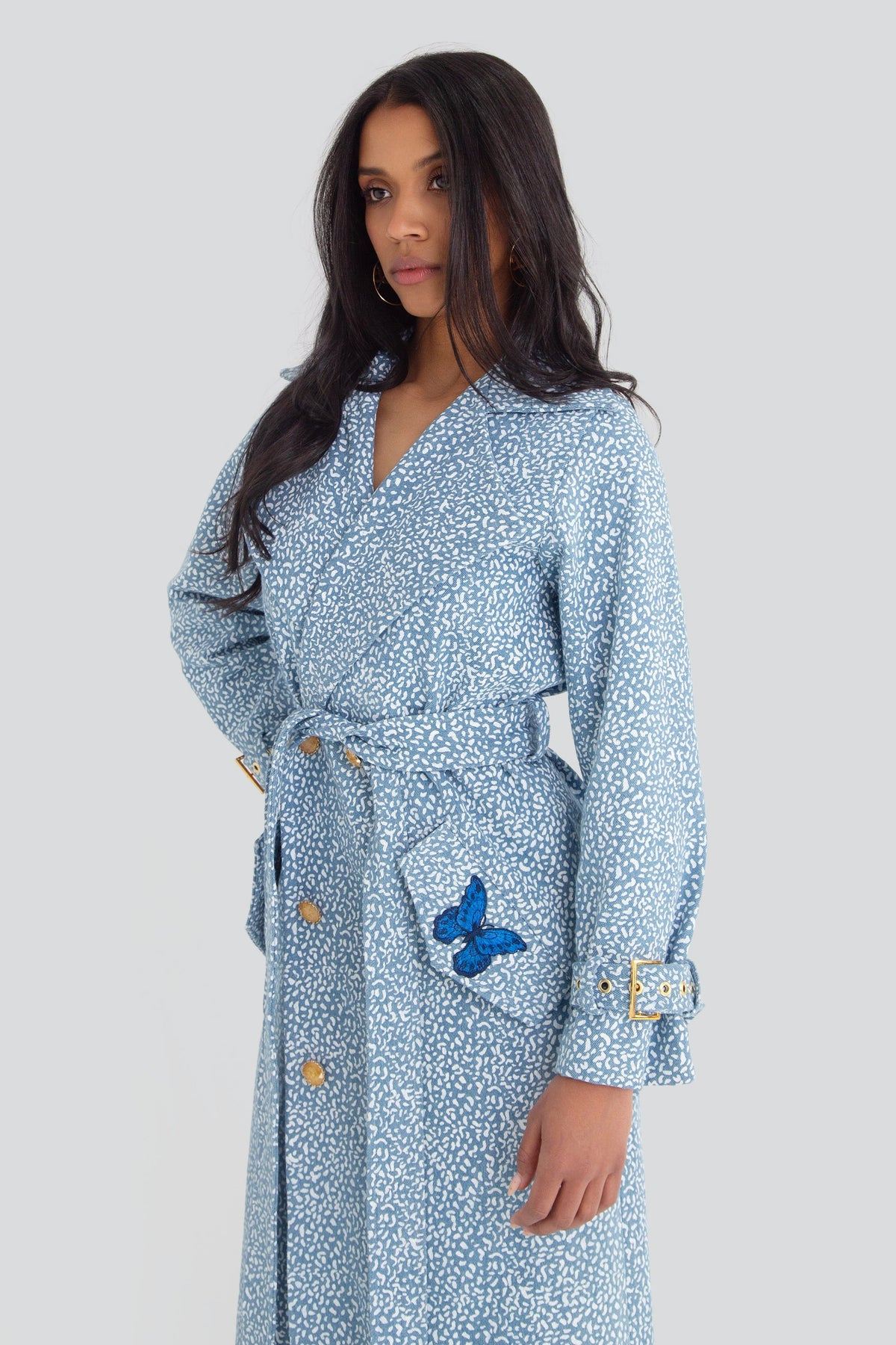 Model styling a luxury light blue patterned denim duster jacket with gold hardware accents in an elegant streetwear outfit