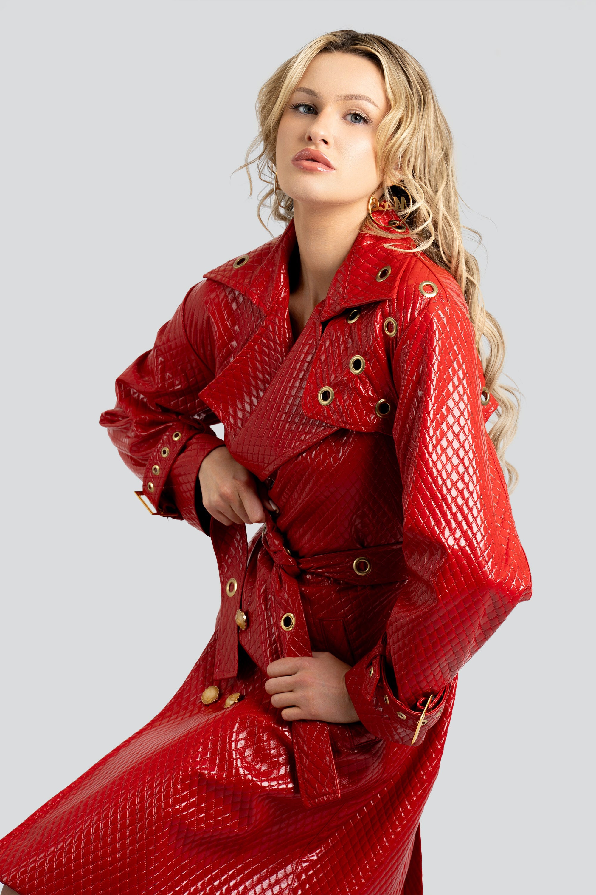 Woman wearing a quilted red trench coat with a belt and gold accents on a white background