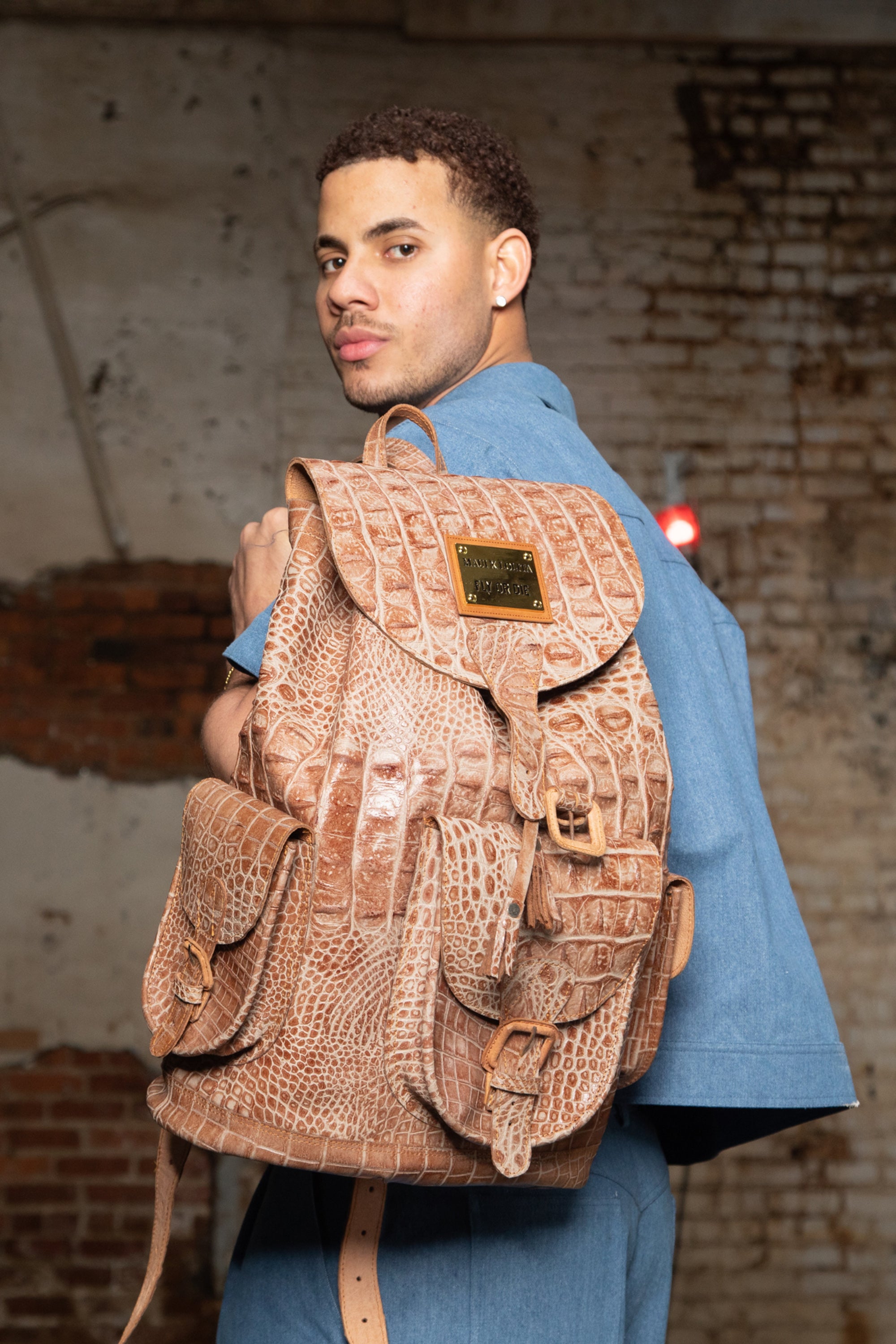 Man wearing a brown leather backpack with a textured pattern against a brick wall.