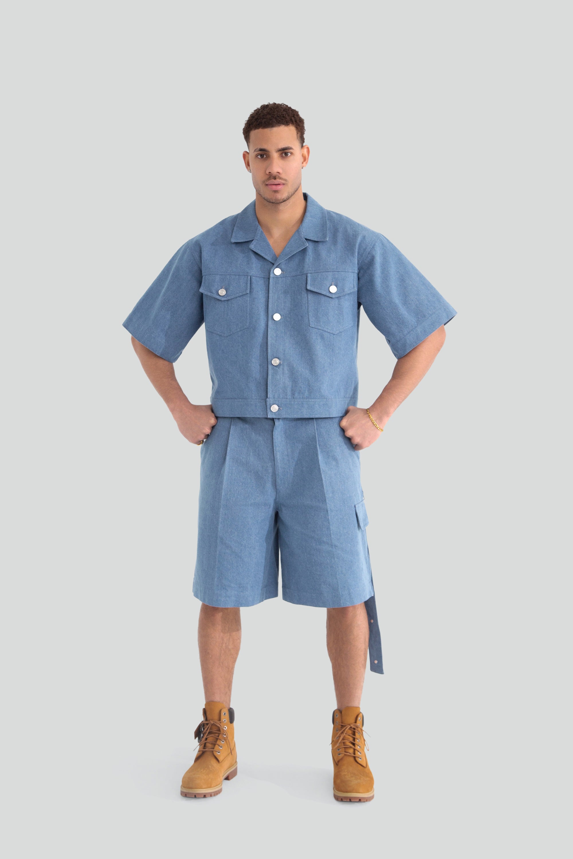Man wearing a denim work shirt and shorts on a plain background