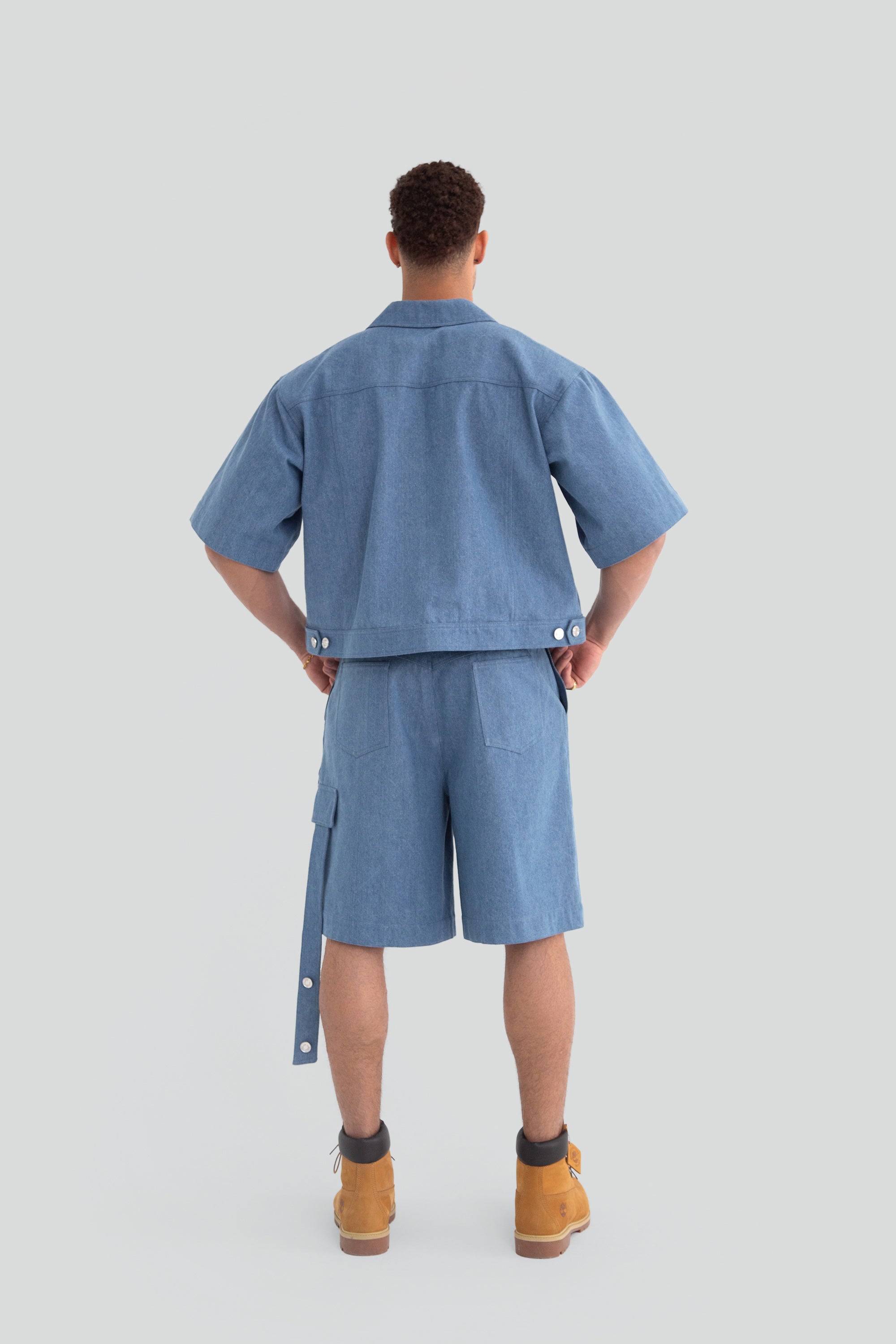 Man wearing a denim work shirt and shorts on a plain background