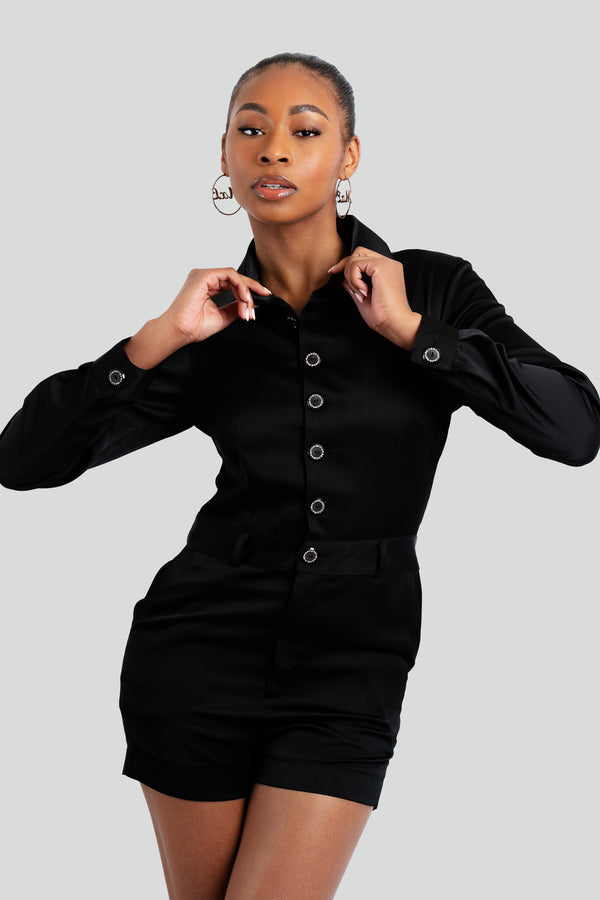 One-piece women's short romper in a rich black tailored fabric, featuring a sharp button-up front, jewel button accents, and a cinched waistband