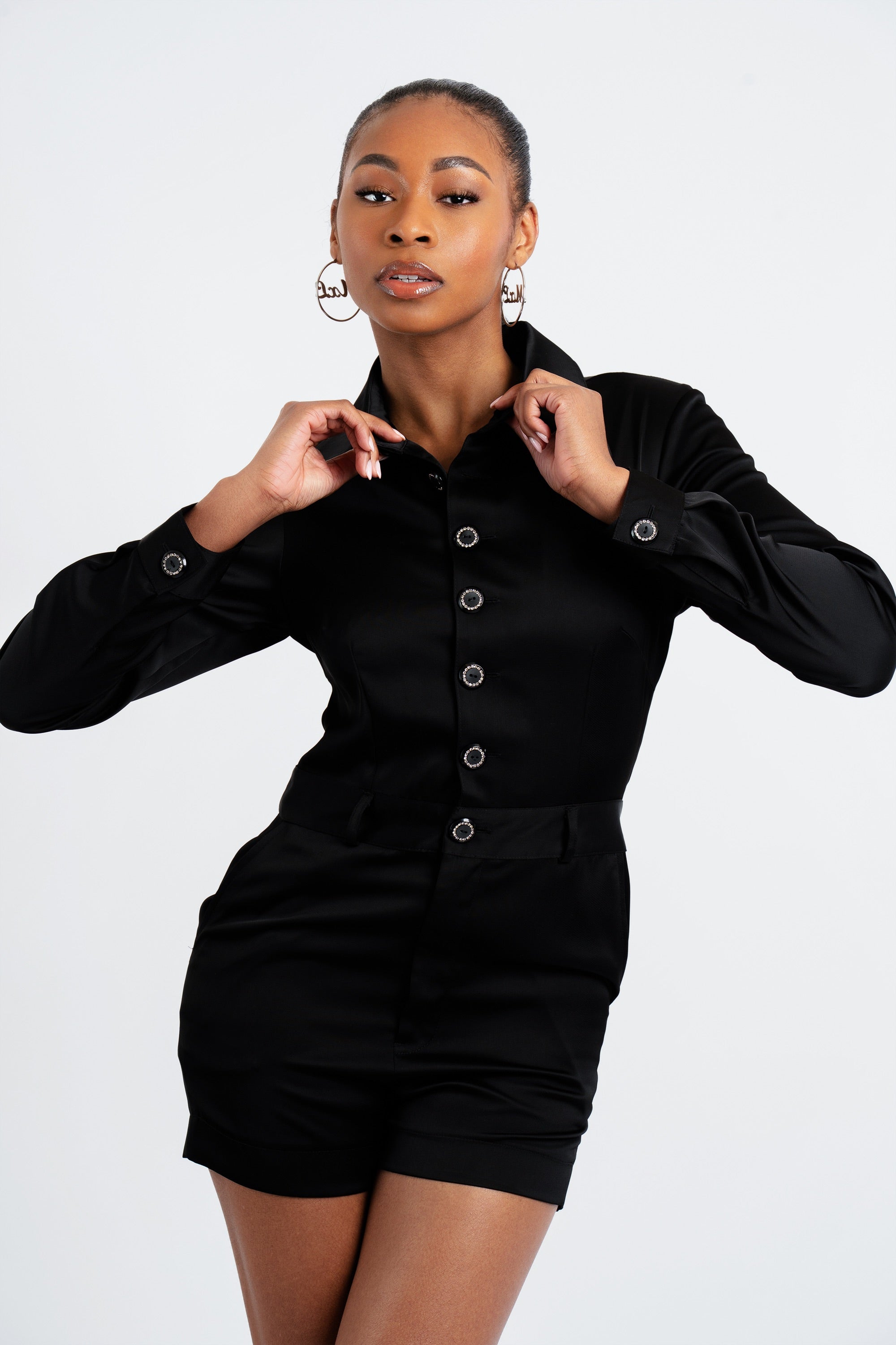 Woman in a black satin romper posing against a white background