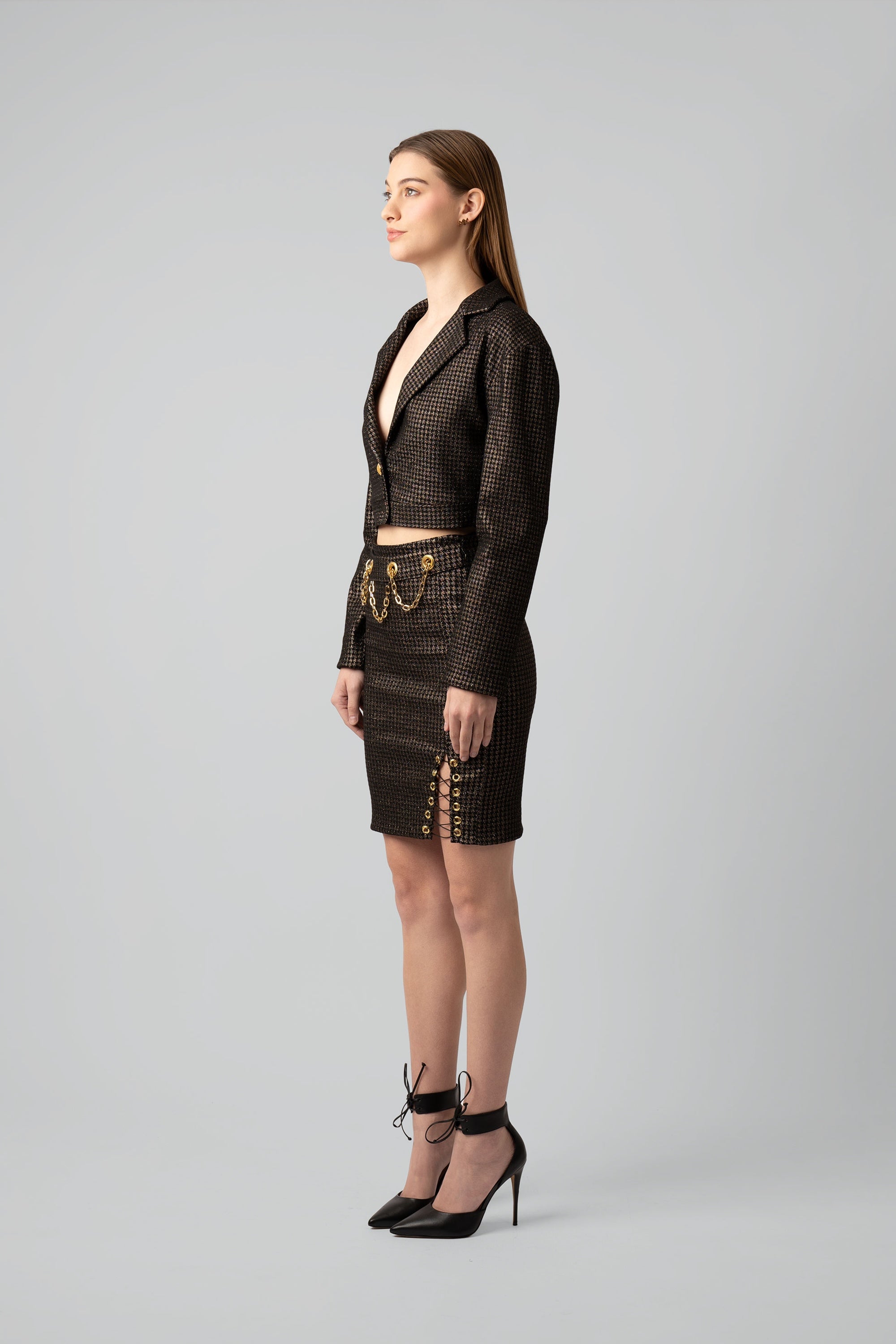 Woman wearing a brown and gold cropped blazer and skirt set with gold accents on a white background