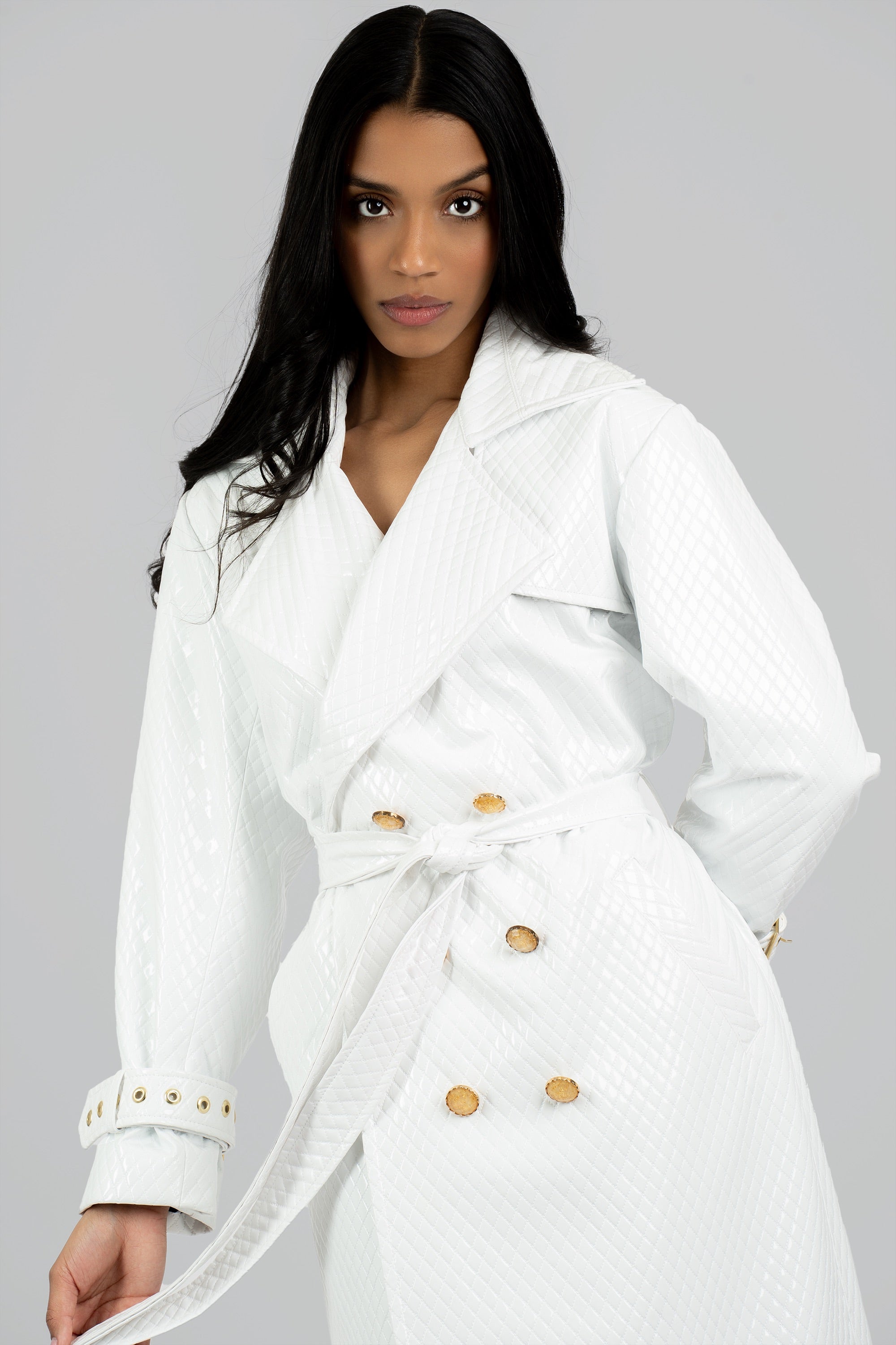 Woman wearing a white trench coat with gold buttons on a gray background
