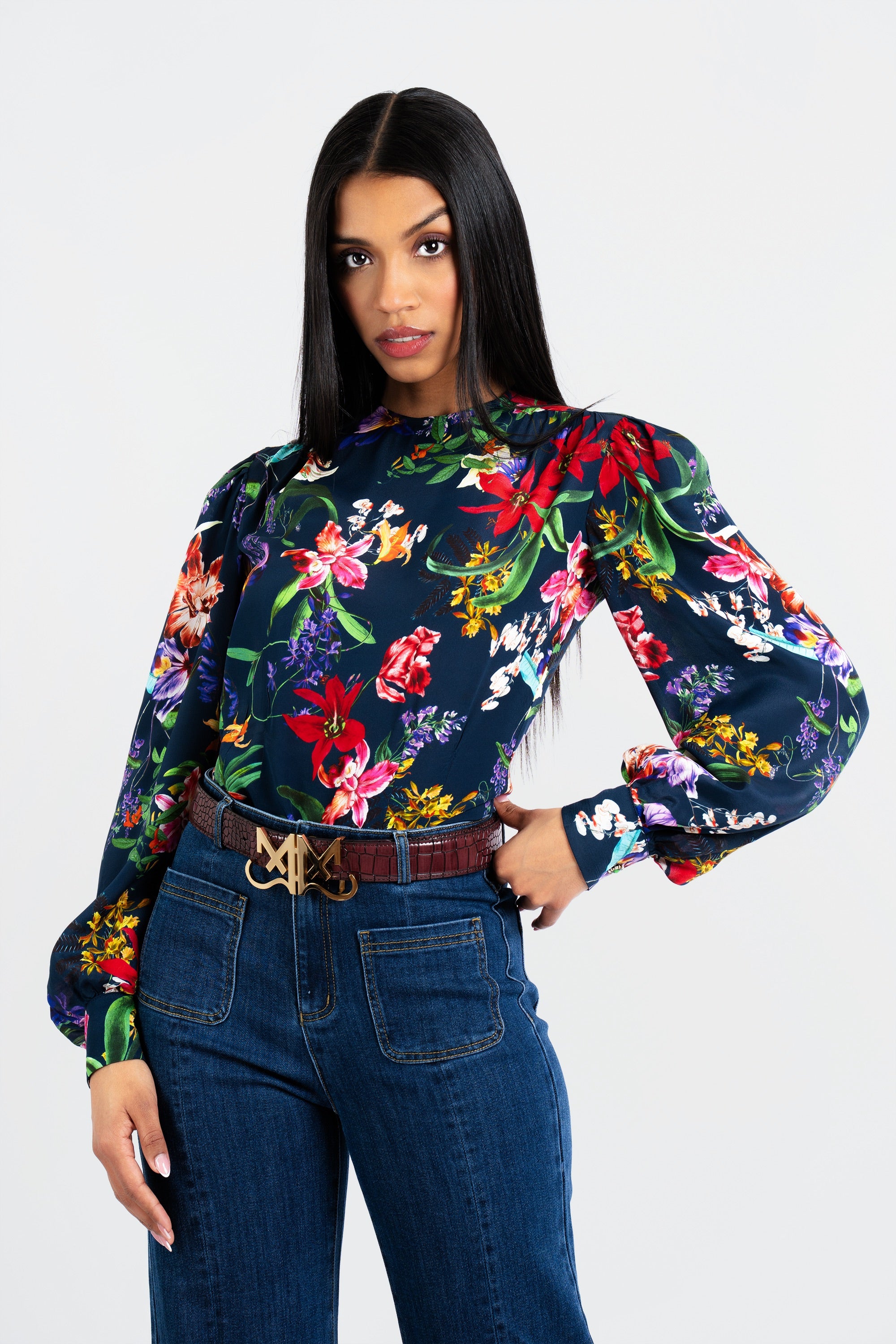 Woman wearing a colorful floral blouse and blue jeans on a white background