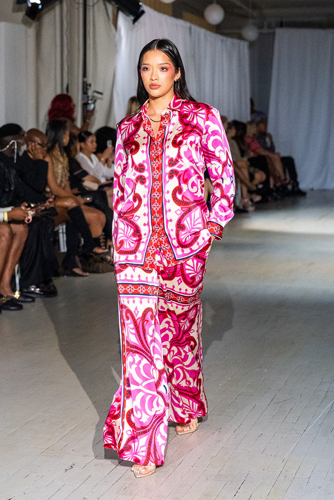 Model wearing a vibrant pink and white patterned outfit on a runway with an audience.