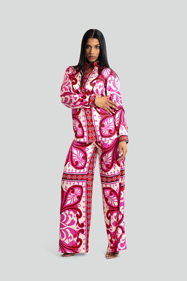 Two-piece women's loungewear set in glossy pink poly-satin fabric, featuring a relaxed button-down shirt and matching wide-leg trousers covered in an ornate fuchsia, crimson, and ivory baroque pattern