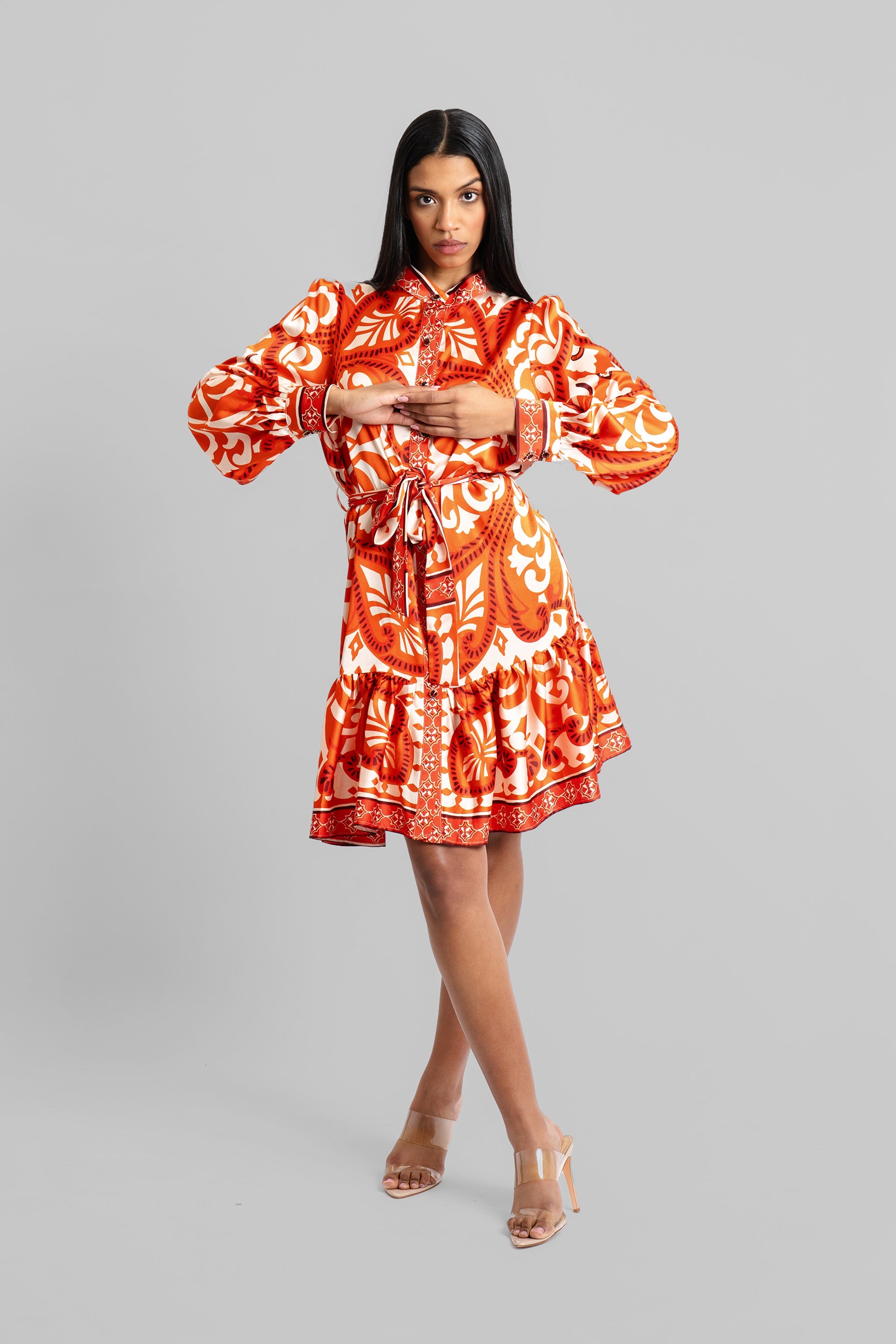 Woman wearing an orange and cream baroque-inspired print dress with voluminous sleeves and cinched waist posing against a white background