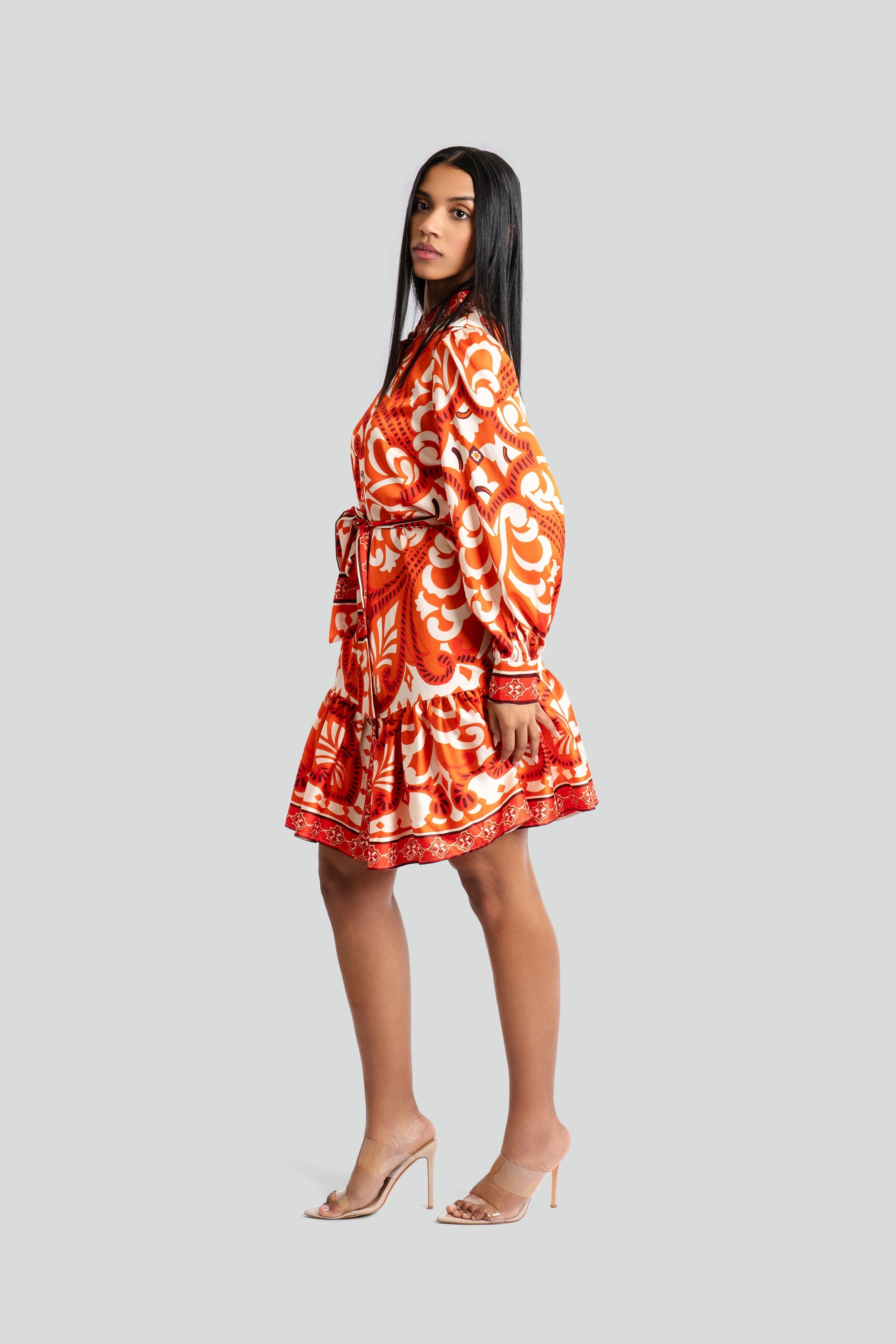 Woman wearing an orange and cream baroque-inspired print shirt dress by Maui X Lolita, showcasing jewel-detailed button closure and a tiered satin-finish skirt