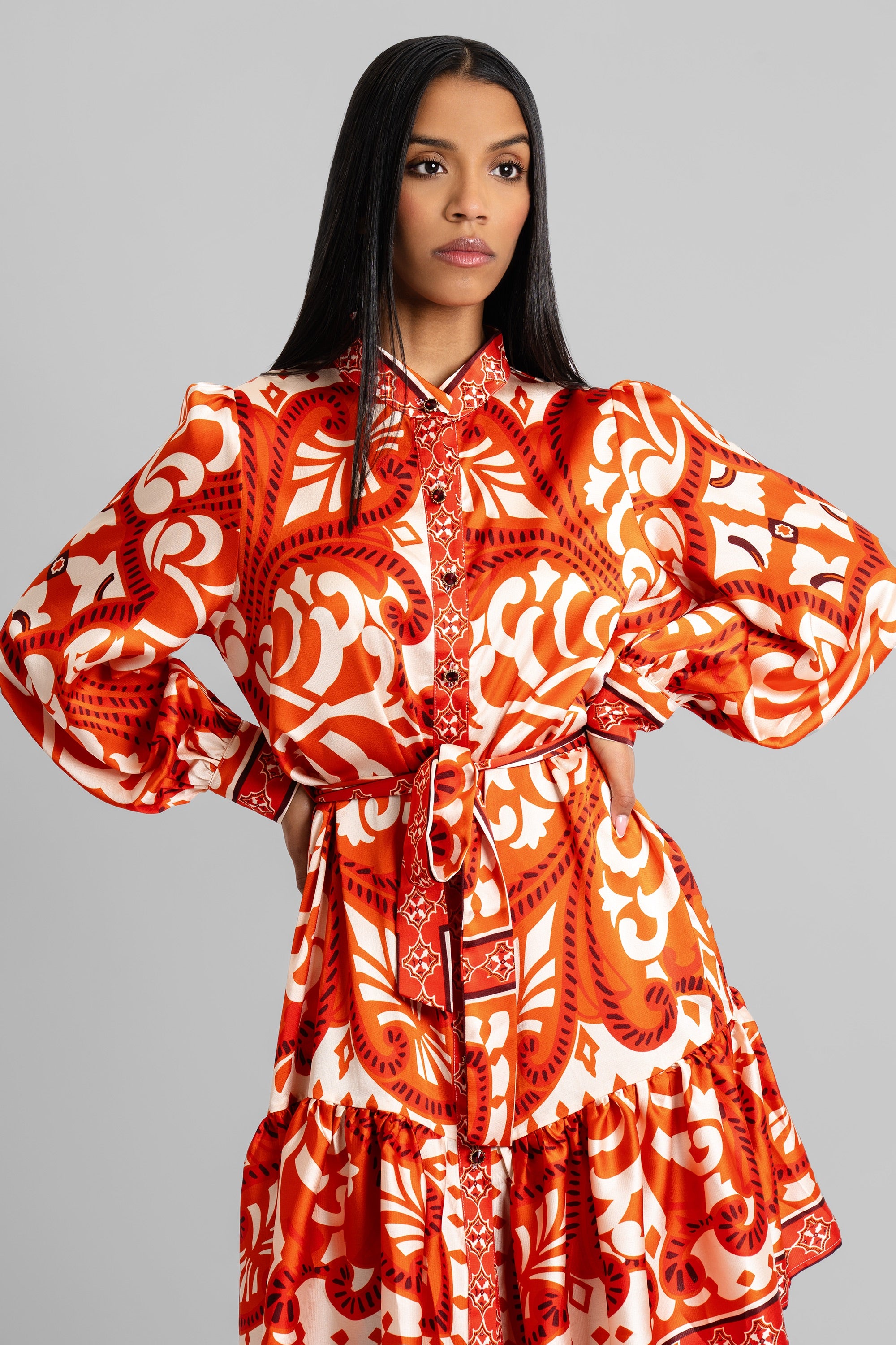 Woman wearing an orange and cream baroque-inspired print dress with voluminous sleeves and cinched waist posing against a white background